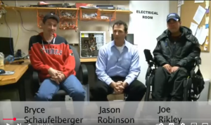 Three men are sitting in an office labeled Electrical Room. The man on the left wears a red sweatshirt, the man in the middle wears a dress shirt, and the man on the right is in a wheelchair. Their names are Bryce, Jason, and Joe.